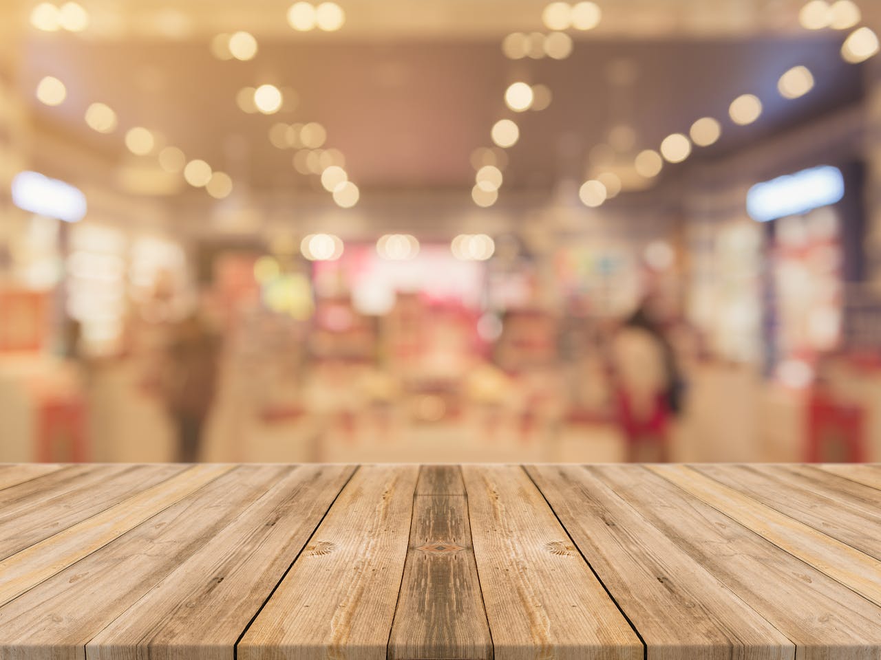 Empty wooden table with blurred shopping mall background and bokeh lights.